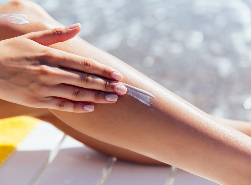 Woman in swimsuit puts sunscreen on her leg, on the beach